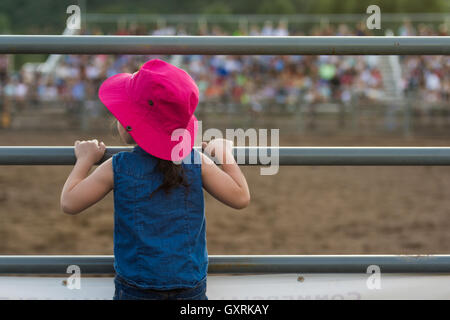 Jeune fille portant un chapeau rose à travers une clôture à un rodéo Banque D'Images