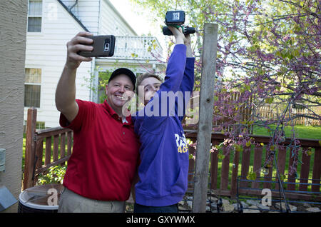 Papa en tenant un téléphone cellulaire pendant que son fils adolescent selfies travaille sur de percer le trou dans la plate-forme pôle d'éclairage. St Paul Minnesota MN USA Banque D'Images