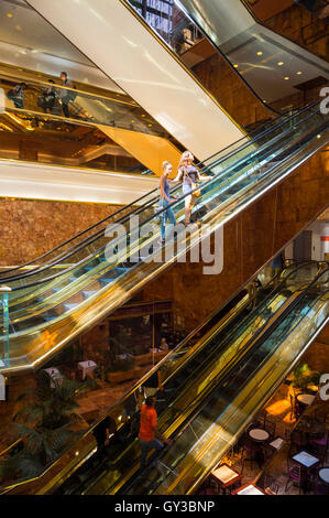 NEW YORK - 3 septembre 2016 : les visiteurs monter les escaliers mécaniques en laiton en miroir dans l'atrium de marbre rose la Trump Tower. Banque D'Images