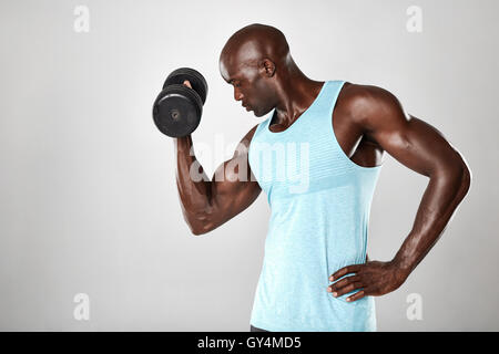 Coup de jeune homme musclé accomplir un exercice d'haltères pour biceps. Modèle de remise en forme de l'Afrique de l'élaboration avec haltères sur gris ba Banque D'Images