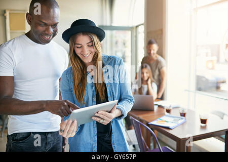 Bel homme noir de la saisie d'informations sur l'ordinateur tablette tenue devant lui par de jeunes femmes adultes en chapeau noir en café hou Banque D'Images