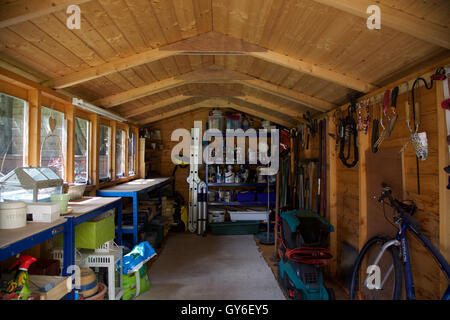 À l'intérieur de l'abri de jardin en bois avec toit avec workbench outils suspendus et des étagères tondeuse serre avec de la peinture et de bain Banque D'Images