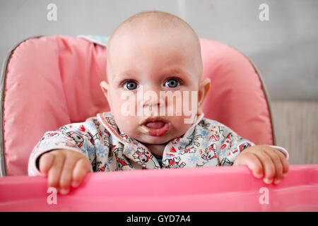 Beau Bébé mange du gruau de Mom's main. Il est assis sur une chaise rose enfants'. Banque D'Images