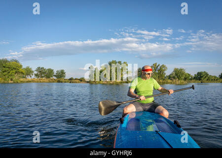 Musclé, senior male pagayeur assis sur un stand up paddleboard sur un lac dans le Colorado Banque D'Images