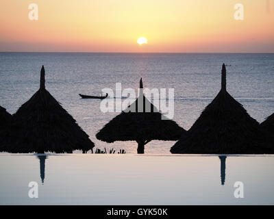 Avis de soleil parasols en chaume silhouetté contre le soleil sur une mer tropicale Banque D'Images