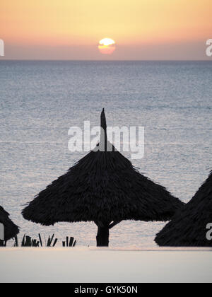 Vue d'un parapluie par soleil chaume silhouetté contre le soleil sur une mer tropicale Banque D'Images