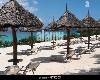 Voir le long d'une rangée de soleil parasols en chaume sur une plage de sable blanc contre un ciel bleu Banque D'Images