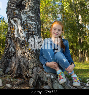 Petite fille assise dans les bois près de Birch. Banque D'Images