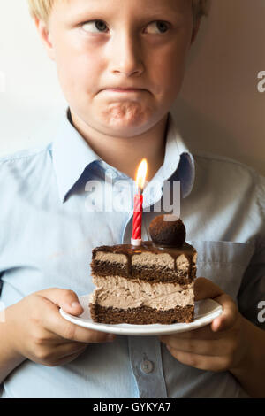 Triste confus enfant (garçon, enfant, adolescent) avec anniversaire gâteau au chocolat avec bougie brûlante - malheureux plate parti, maison de vacances, birthd Banque D'Images