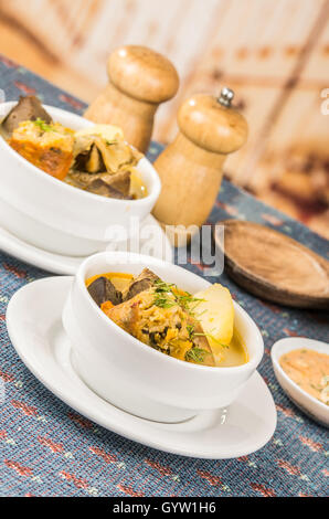 Classy servant de soupe de pommes de terre avec de la viande et légumes, servis dans des bols blancs assis sur table, nappe bleue, sel poivre shakers, agréable restaurant background Banque D'Images