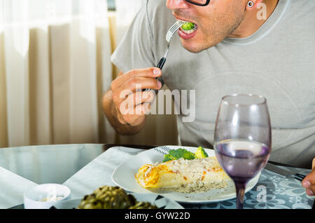Homme assis en classe pour le dîner manger avec la fourchette du brocoli, des couverts de crêpe en sauce blanche située sur la plaque Banque D'Images