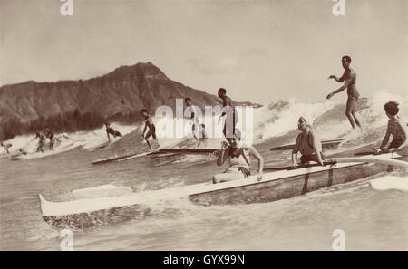 Vue sur les vagues de Waikiki, Honolulu, avec des hommes sur des planches de surf en bois et des femmes dans un bateau à outrigger. Photo de Tom Blake, 1931. Banque D'Images