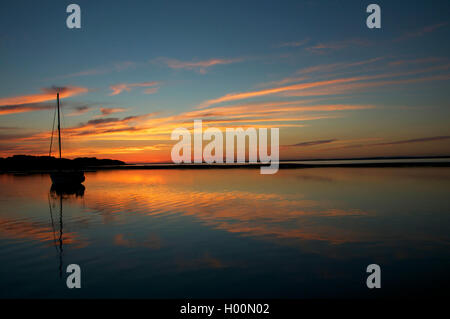 Location de bateaux sur l'eau calme silhouetté contre frappant le coucher du soleil. Banque D'Images