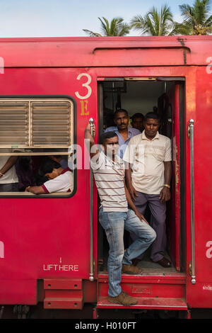 HIKKADUWA, SRI LANKA - le 22 février 2014 : Les gens debout dans le train de la porte. Prendre le train est un excellent moyen de s'aro Banque D'Images