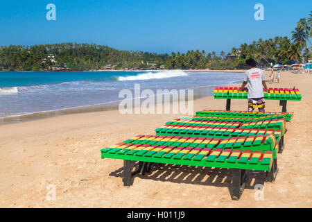 UNAWATUNA, SRI LANKA - 6 mars, 2014 : travailleur local mettre des chaises longues en bois colorés sur la plage. Unawatuna est une importante Banque D'Images