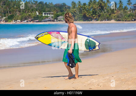 UNAWATUNA, SRI LANKA - 6 mars, 2014 : Jeune homme marche sur une plage de sable de planche de surf. Unawatuna est bien connu entre tourisme Banque D'Images