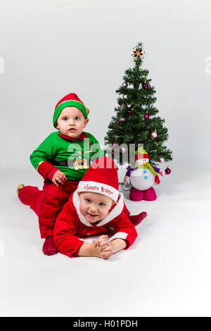 Deux garçons de bébé habillé en père Noël et Santa's Helper couché à côté d'arbre de Noël. Arrière-plan blanc. Banque D'Images