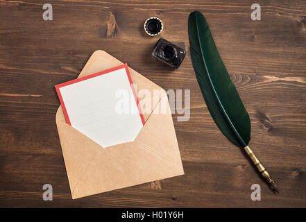 Enveloppe avec carte vide et plume sur table en bois Banque D'Images