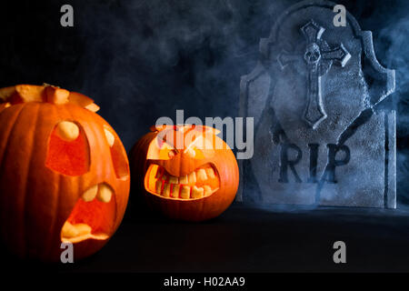 Peur et visage en colère face à des citrouilles d'halloween avec pierre tombale sur misty fond sombre. Banque D'Images