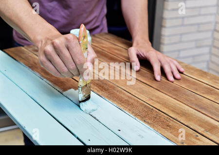 Libre d'un young caucasian man painting une vieille table en bois avec un pinceau Banque D'Images