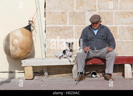 MARSAXLOKK, MALTE - 11 janvier 2015 : un homme âgé avec chien assis sur le banc de la rue. Banque D'Images