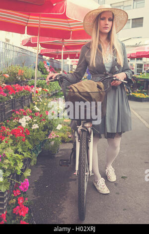 Belle fille blonde avec chapeau de paille et le vélo sur la place de marché. Poste a traité avec filtre vintage. Banque D'Images