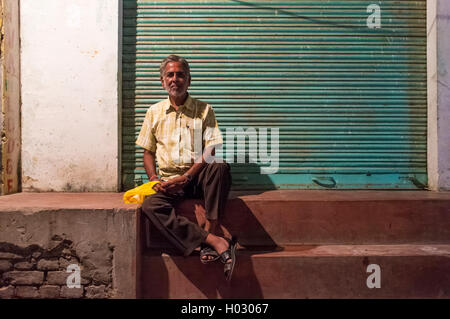 VARANASI, INDE - 19 février 2015 : l'homme est assis en face de magasin fermé. Banque D'Images