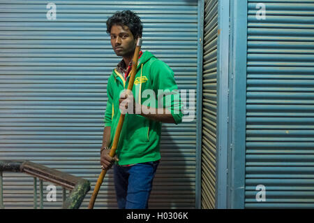 VARANASI, INDE - 20 février 2015 : Jeune homme Indien détient à balai et se trouve à côté de magasins fermés. Banque D'Images