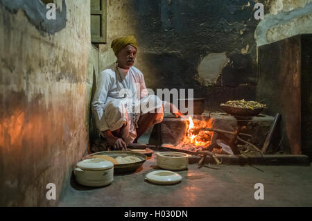 Région GODWAR, INDE - 12 février 2015 : Indian homme vêtu de vêtements traditionnels rend chapati sur feu ouvert dans la cuisine ancienne. Ch Banque D'Images