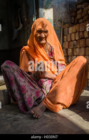 Région GODWAR, INDE - 13 février 2015 : personnes âgées femme indienne en sari avec tête couverte est assis dans la porte de la maison. Banque D'Images