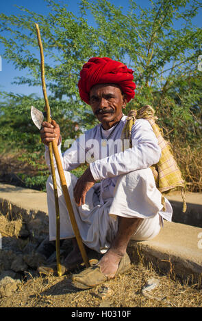 Région GODWAR, INDE - 14 février 2015 : personnes âgées Rabari tribesman avec turban rouge est assis et tient une hache et s'en tenir. Rabari ou Rewari Banque D'Images