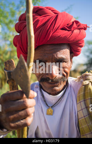 Région GODWAR, INDE - 14 février 2015 : personnes âgées Rabari tribesman avec turban rouge est assis et tient une hache et s'en tenir. Rabari ou Rewari Banque D'Images