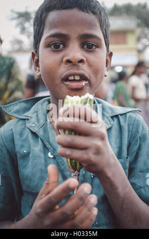 KAMALAPURAM, INDE - 02 février 2015 : jeune garçon indien mange un légume sur un marché proche de Hampi. Post-traités avec grain, Banque D'Images