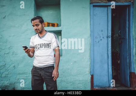 KAMALAPURAM, INDE - 02 février 2015 : Indian homme regarde son téléphone portable à l'extérieur de sa maison. Post-traités avec grain, texture Banque D'Images