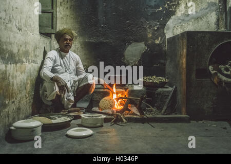 Région GODWAR, INDE - 12 février 2015 : Indian homme vêtu de vêtements traditionnels rend chapati sur feu ouvert dans la cuisine ancienne. Po Banque D'Images