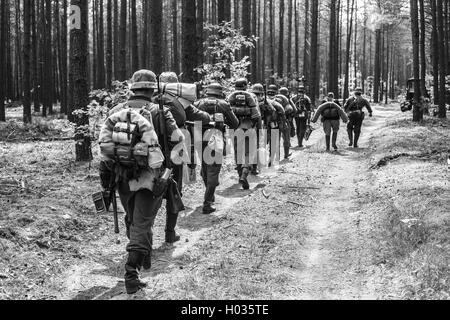 Des reconstitutions historiques non identifiés habillés en soldats allemands de la Seconde Guerre mondiale marche sur route forestière. La Photographie noir et blanc Banque D'Images