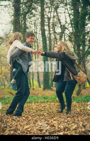 Manèges fille père sur piggyback avec mère à côté d'eux dans le parc une journée d'automne. Banque D'Images