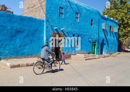 Louxor, Egypte - 11 février 2016 : Kid et cycliste en passant par la maison typique. Banque D'Images