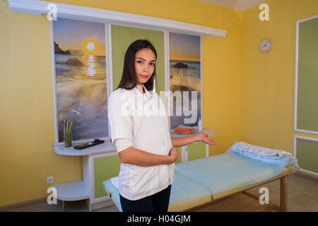 Esthéticienne souriante debout à côté de la table de massage au spa et accueille le client invite Banque D'Images
