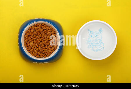 Aliments secs pour chats marron en partie avec bol en céramique bleu et de l'eau mot cat en blanc sur jaune marbre, Close up, vue du dessus, les p Banque D'Images