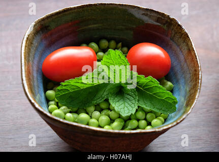 Les petits pois frais à la menthe et les tomates dans la main-bol poterie jeté Banque D'Images