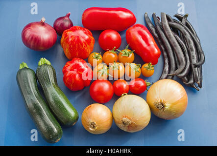 Arrangement d'un assortiment de variétés de tomates fraîchement cueillies, et autres légumes du jardin d'été, sur un fond bleu. Banque D'Images