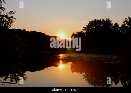 Un coucher de soleil d'été dans le Michigan pure, avec un reflet du lac des arbres et du soleil dans le parc Banque D'Images