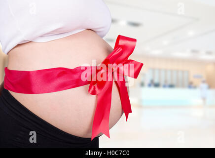 Close up femme enceinte avec ruban rouge sur le ventre de cadeaux à l'hôpital historique Banque D'Images
