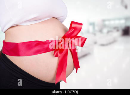 Close up femme enceinte avec ruban rouge sur le ventre de cadeaux à l'hôpital historique Banque D'Images