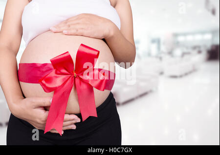 Close up femme enceinte avec ruban rouge sur le ventre de cadeaux à l'hôpital historique Banque D'Images