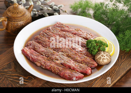 Tranches de boeuf assaisonné sur plaque blanche avec du citron, des herbes et champignons Banque D'Images