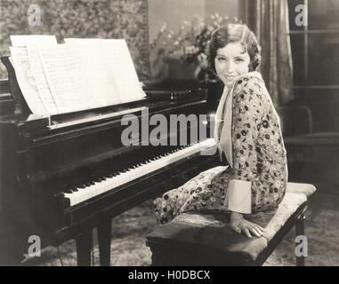 Smiling woman sitting by piano à la maison Banque D'Images