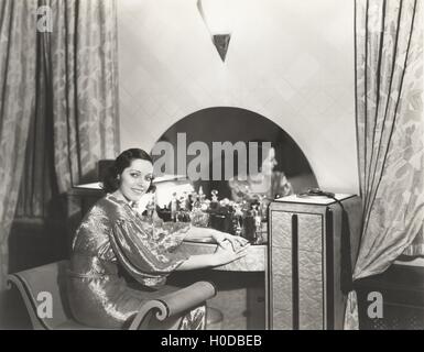 Femme en robe métallique assise à sa coiffeuse Banque D'Images
