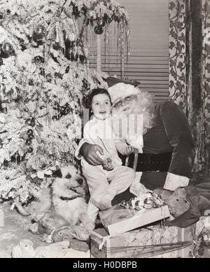 Petite fille assise sur les genoux du Père Noël en vertu de l'arbre de Noël Banque D'Images